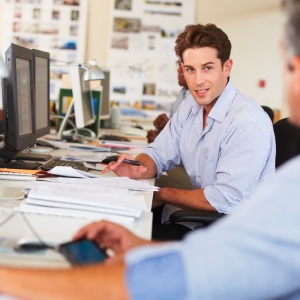 Two coworkers discussing documents at office desks